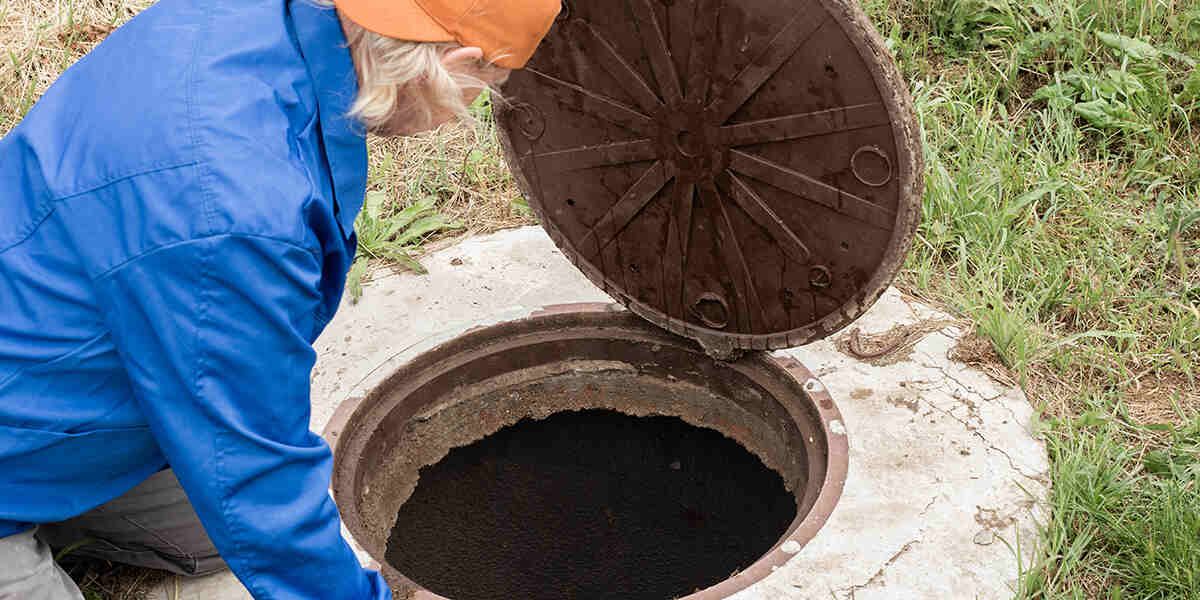 Worker in blue jacket opening a manhole cover to inspect a sewer opening